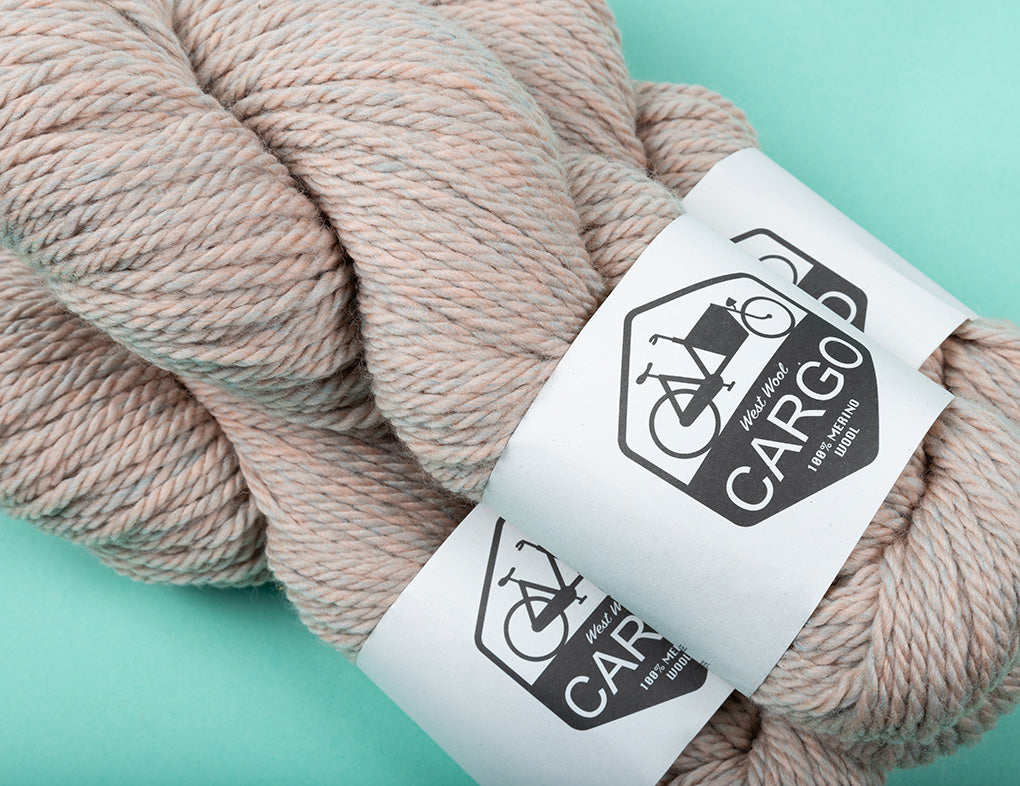 This image shows three skeins of West Wool Cargo in a heathered cream colour, on a pastel green background. 