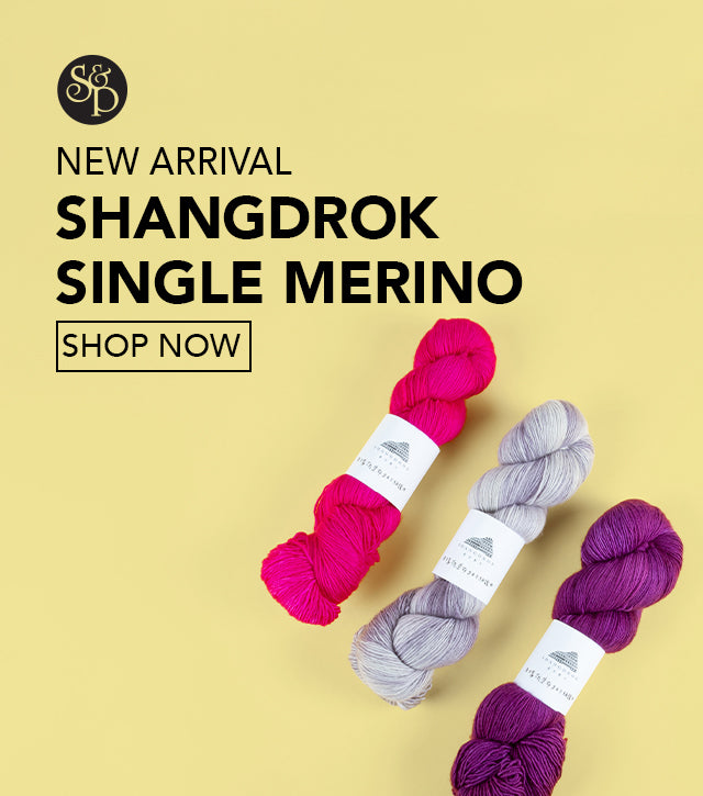 This image advertises that the base "Single Merino" from the brand Shangdrok has newly arrived at Stephen & Penelope. The text includes a "shop now" button and the S&P black logo. The image shows three skeins of Shangdrock yarn in pink., grey, and purple on a light yellow background. 